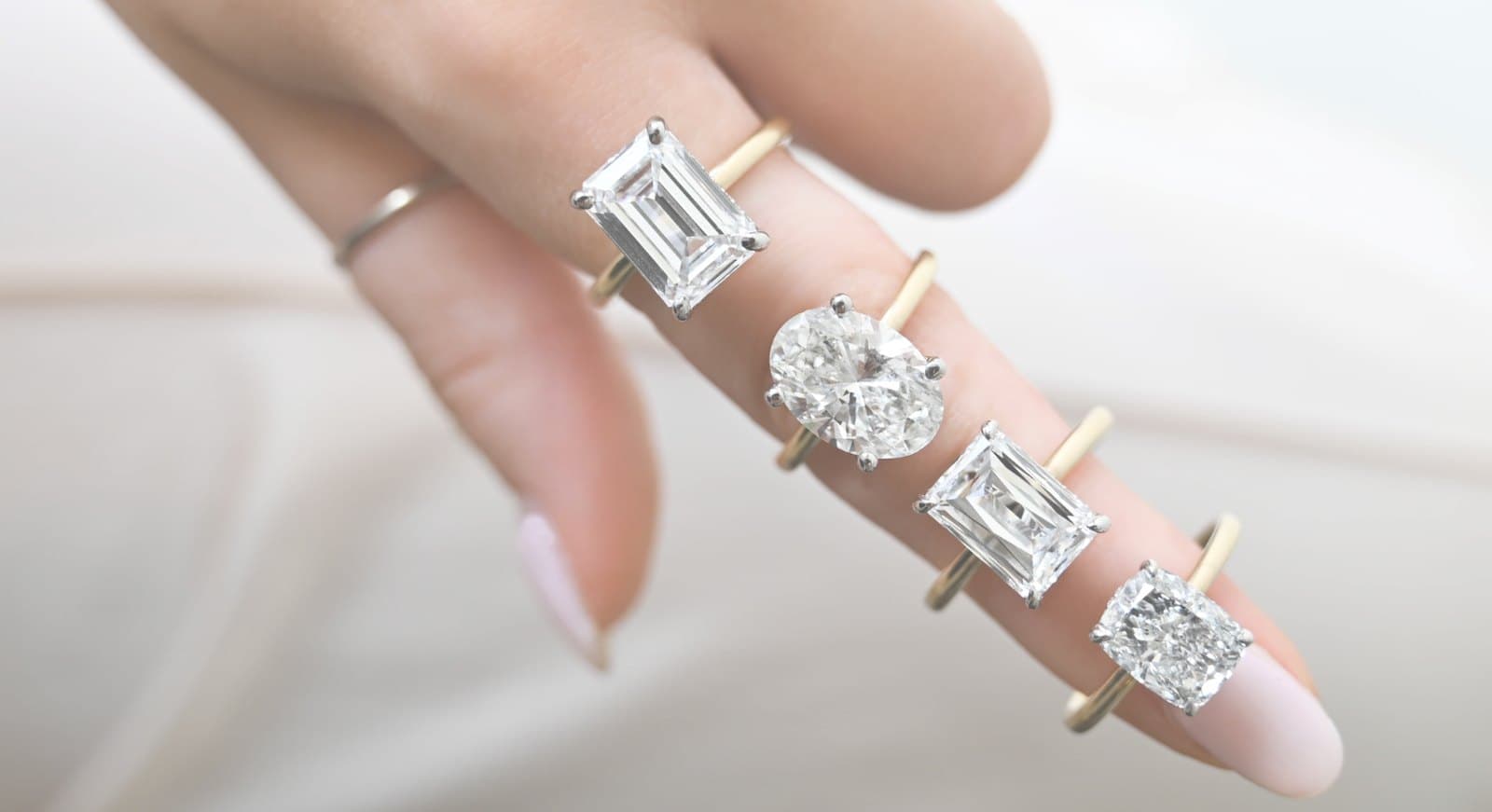 Emerald, oval, radiant and cushion diamonds on yellow-gold solitaire settings held on a hand